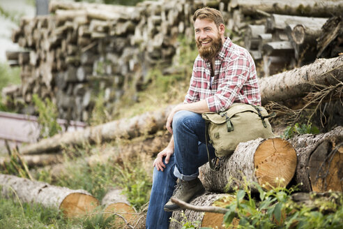 Lachender bärtiger Mann sitzt auf einem Holzstapel - MAEF12378