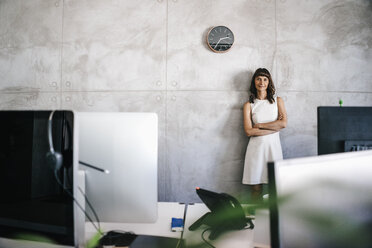 Businesswoman standing under wall clock with arms crossed - KNSF01995