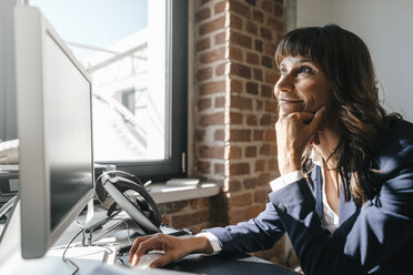 Business woman sitting at desk, looking onto sunlight - KNSF02016