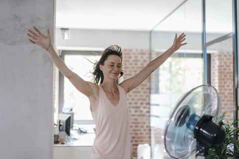 Geschäftsfrau im Büro genießt Brise aus einem Ventilator, lizenzfreies Stockfoto