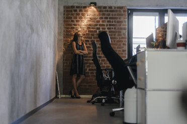 Geschäftsfrau steht mit verschränkten Armen im Büro und schaut auf eine Lampe - KNSF02059