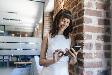 Businesswoman standing in office, holding smartphone - KNSF02077