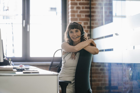 Frau sitzt im Büro und trägt ein Headset, lizenzfreies Stockfoto