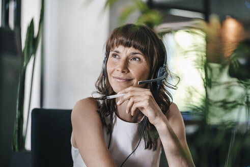 Woman sitting in office, wearing headset - KNSF02082
