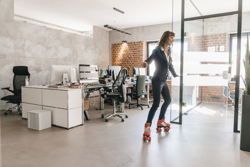 Successful businesswoman wearing roller skates in office - KNSF02090