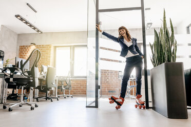 Successful businesswoman wearing roller skates in office - KNSF02091
