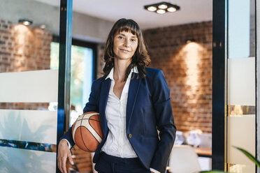 Businesswoman holding basket ball in office - KNSF02100