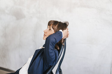 Businesswoman sitting in chair, with hands behind head, thinking - KNSF02101