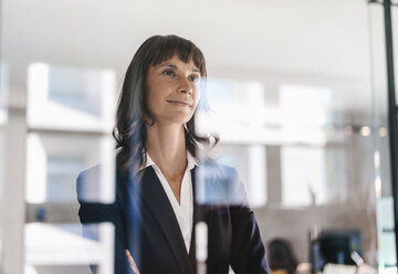 Successful businesswoman looking through glass pane - KNSF02104