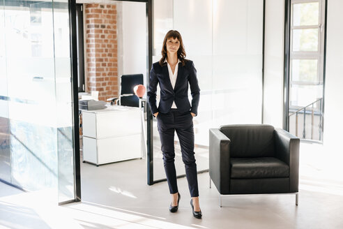 Successful businesswoman standing in office with hands in pockets - KNSF02105