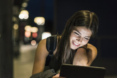 Porträt einer jungen Frau mit Kopfhörern und Tablet, die am nächtlichen Bahnhof wartet - UUF11065