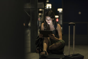 Lächelnde junge Frau mit Tablet wartet am Bahnhof bei Nacht - UUF11066
