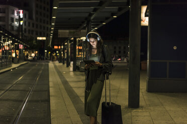 Junge Frau mit Kopfhörern und Tablet wartet nachts am Bahnhof - UUF11074
