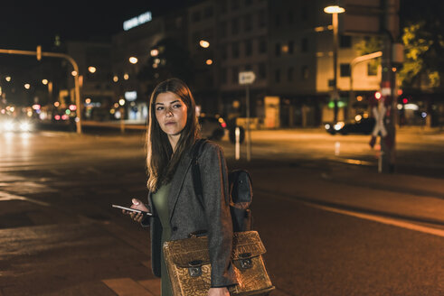 Porträt einer jungen Geschäftsfrau mit Gepäck und Mobiltelefon bei Nacht - UUF11080