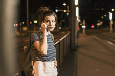 Portrait of young woman on the phone waiting at station by night - UUF11094