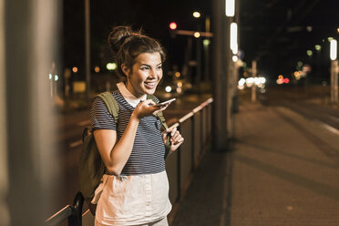 Porträt einer jungen Frau am Telefon, die am nächtlichen Bahnhof wartet - UUF11095