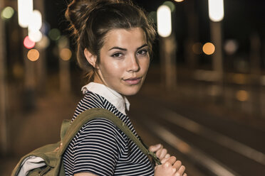 Porträt einer jungen Frau mit Rucksack, die am nächtlichen Bahnhof wartet - UUF11096