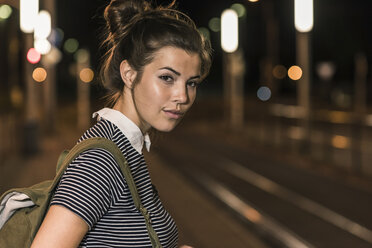 Porträt einer jungen Frau mit Rucksack, die am nächtlichen Bahnhof wartet - UUF11097