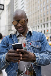 USA, New York City, Manhattan, Porträt eines Mannes mit verspiegelter Sonnenbrille, der auf sein Mobiltelefon schaut - MAUF01167