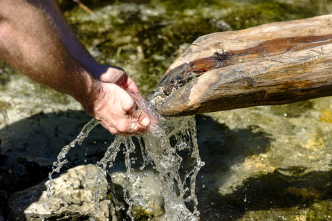 Hände eines Mannes, der Wasser aus einer Quelle trinkt, Nahaufnahme, lizenzfreies Stockfoto