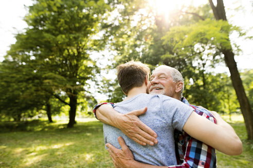 Glücklicher älterer Vater, der seinen erwachsenen Sohn in einem Park umarmt - HAPF01861