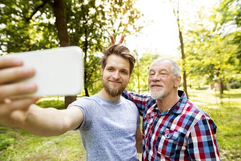 Porträt eines älteren Vaters und seines erwachsenen Sohnes, die ein Selfie in einem Park machen - HAPF01866