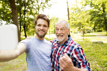 Portrait of senior father and his adult son taking selfie in a park - HAPF01867