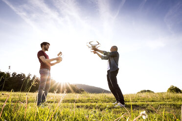 Senior father and his adult son with drone on a meadow - HAPF01873