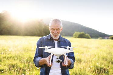 Porträt eines älteren Mannes mit Drohne auf einer Wiese - HAPF01875