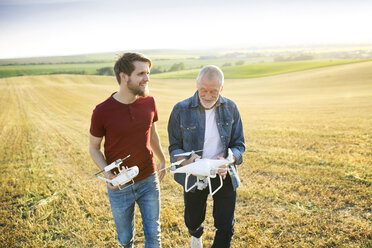 Älterer Vater und sein erwachsener Sohn mit Drohne auf einem Feld - HAPF01880