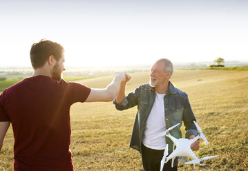 Senior father and his adult son with drone on a field - HAPF01882