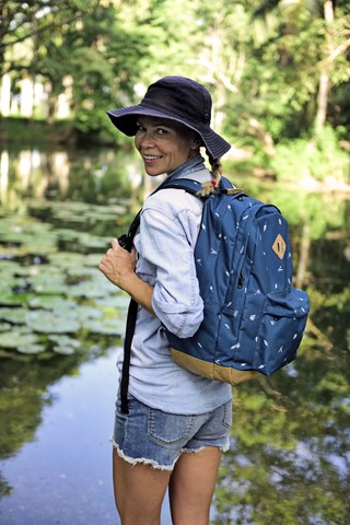 Porträt einer lächelnden Frau mit Rucksack, die vor einem See steht, lizenzfreies Stockfoto