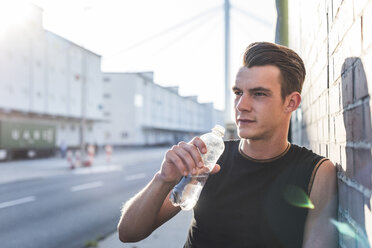 Germany, Mannheim, Young athlete in the city with bottle of water, portrait - UUF11112