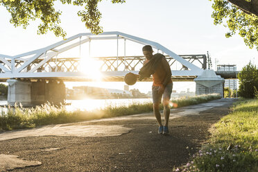 Junger Mann dribbelt Basketball am Fluss - UUF11128