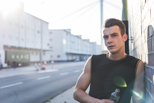 Germany, Mannheim, Young athlete in the city with bottle of water, portrait - UUF11131