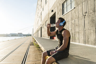 Young athlete wearing headphones, sitting on a wall - UUF11149