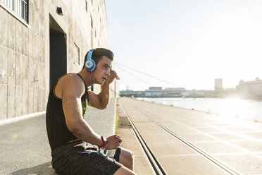 Young athlete wearing headphones, sitting on a wall - UUF11150