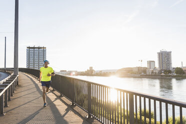 Junger Sportler joggt auf einer Brücke in der Stadt - UUF11158