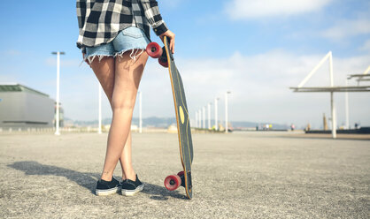 Back view of young woman with longboard in front of beach promenade, partial view - DAPF00766