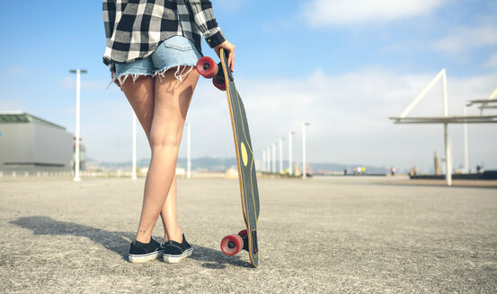 Rückenansicht einer jungen Frau mit Longboard vor einer Strandpromenade, Teilansicht - DAPF00766