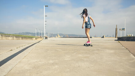 Back view of young woman longboarding on beach promenade - DAPF00771