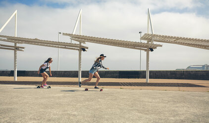 Two young women longboarding on beach promenade - DAPF00776