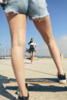 Glückliche junge Frau mit Longboard und Kopfhörern auf der Strandpromenade - DAPF00778