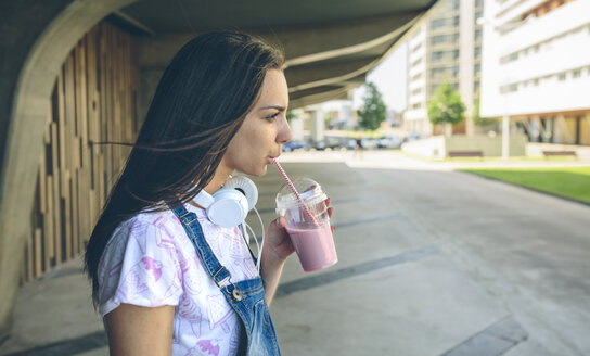 Junge Frau mit Kopfhörern, die einen Erdbeer-Smoothie trinkt - DAPF00791