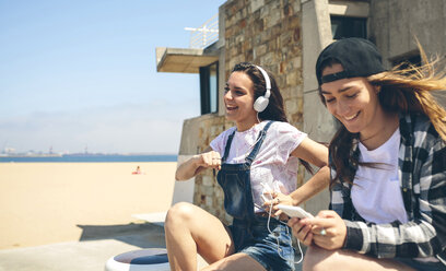 Zwei glückliche junge Frauen hören Musik und haben Spaß am Strand - DAPF00793