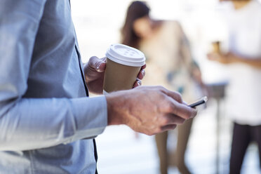 Hand eines Mannes, der eine Tasse Kaffee hält und ein Smartphone benutzt - ZEF14124