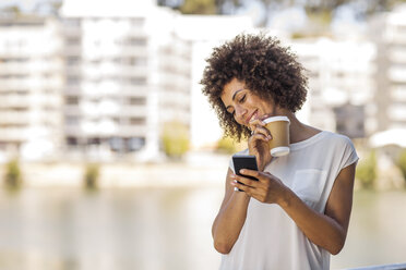 Young woman taking a break outdoors, holding cup of coffee and smartphone - ZEF14131