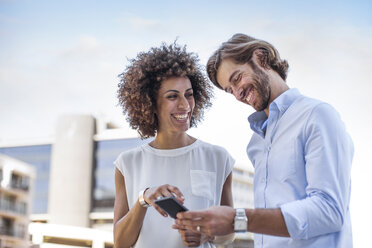 Businessman and woman having a meeting outdoors, using smartphone - ZEF14139