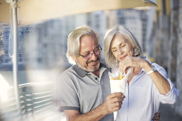 Senior couple taking a city break, eating French fries - ZEF14161