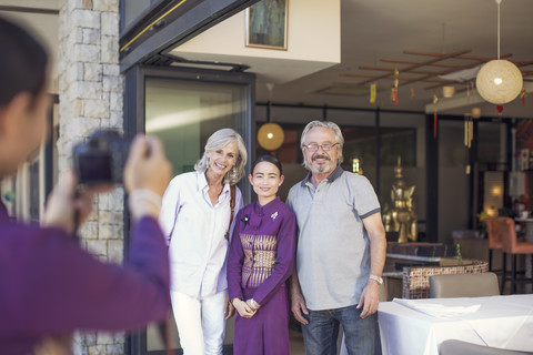 Älteres Paar fotografiert mit asiatischer Kellnerin vor einem Restaurant, lizenzfreies Stockfoto